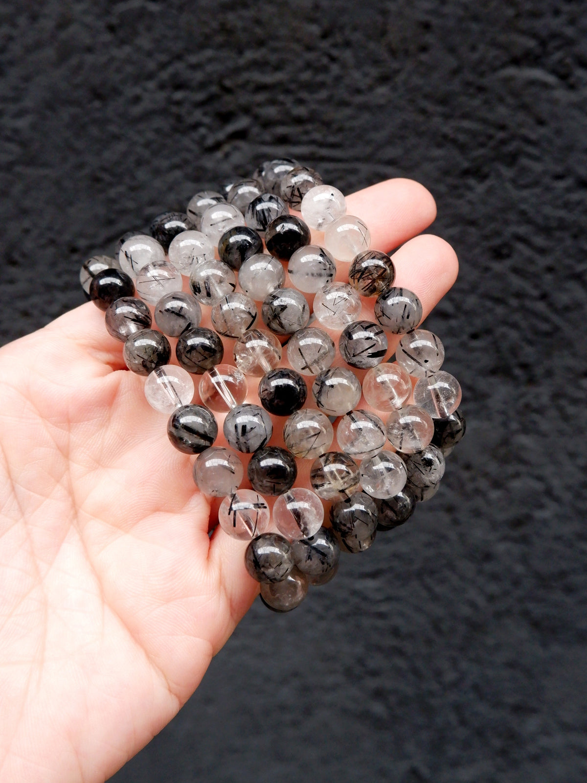 A hand holding a bundle of round clear and black glass beads with visible inclusions, set against a dark textured background.