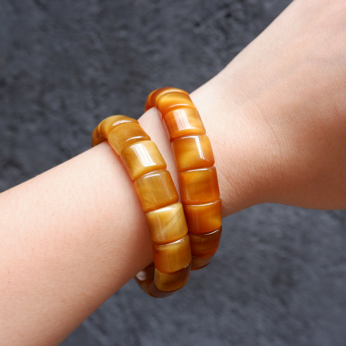 Two chunky amber-yellow beaded bracelets with a glossy finish, worn stacked on a person's wrist against a dark textured background.