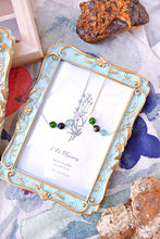 Necklace with green stones displayed in a decorative frame on a textured surface with rocks.