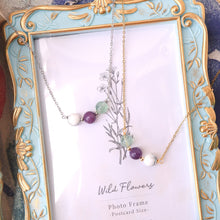 Necklace with purple and white beads on a decorative frame labeled 'Wild Flowers'.