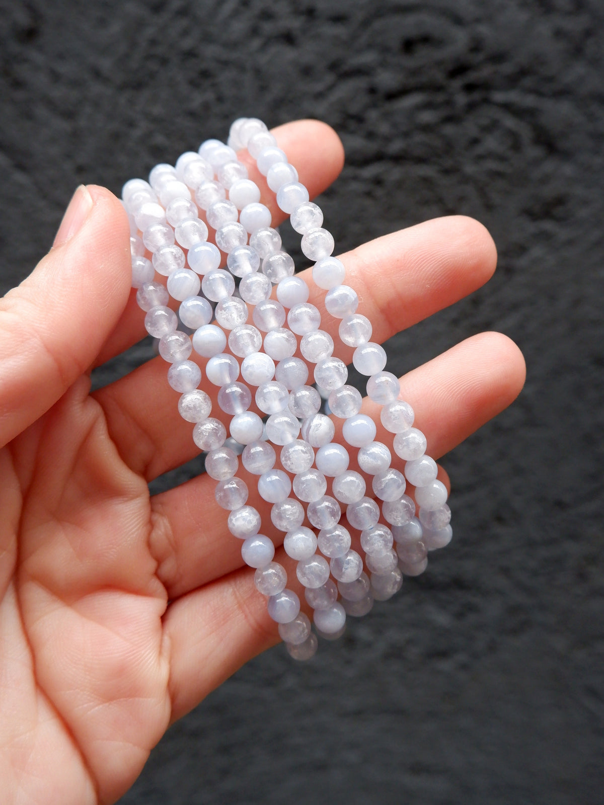 A hand holding a bundle of translucent white beaded bracelets against a dark textured background.