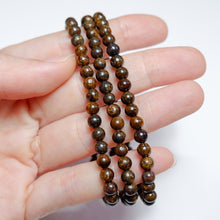 Hand holding a string of brown beaded bracelets on a white background