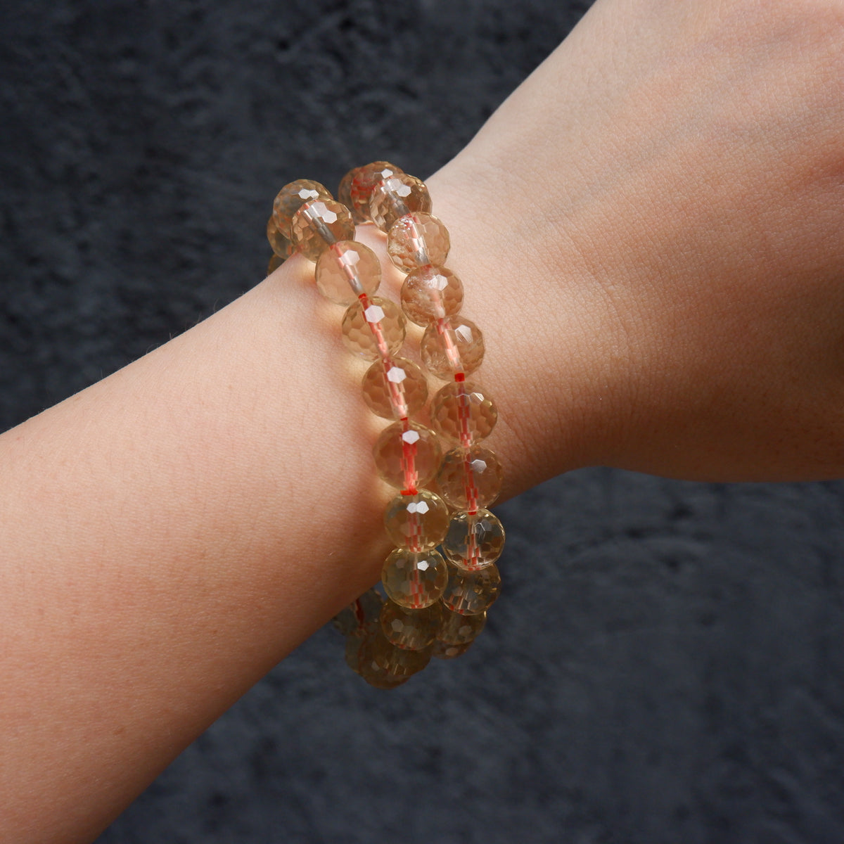 Two beaded crystal bracelets in a warm golden-brown hue worn on a person's wrist against a dark textured background.
