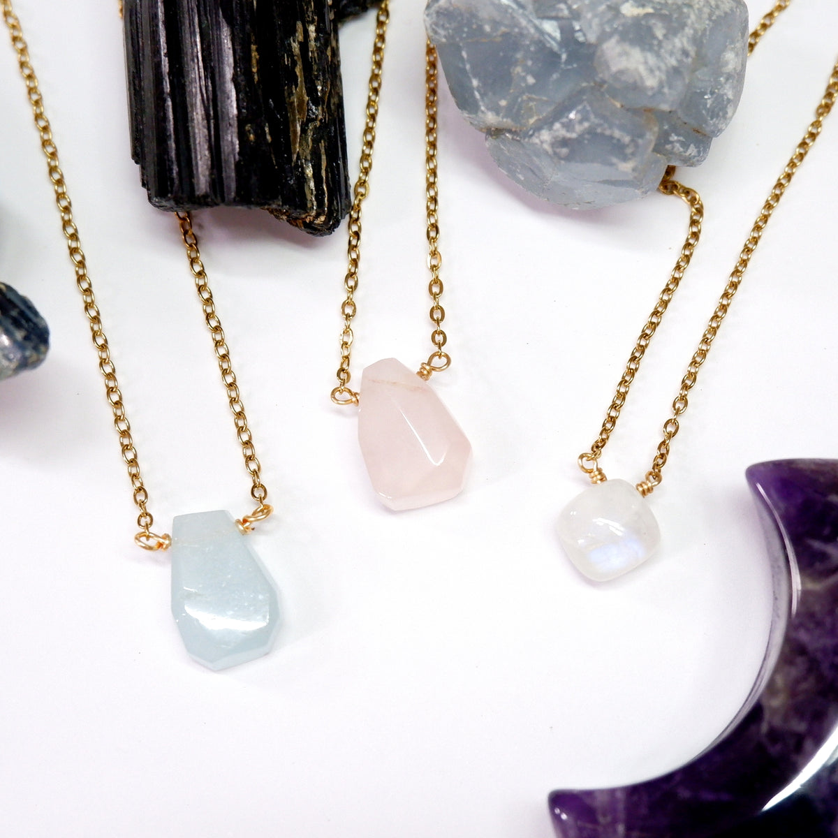 Three gold necklaces with stone pendants on a white surface with crystals.