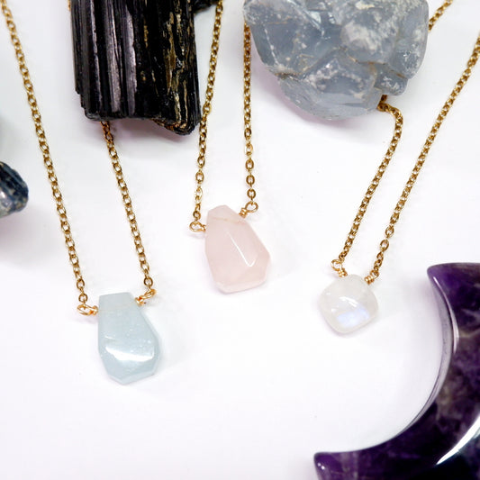 Three gold necklaces with stone pendants on a white surface with crystals.