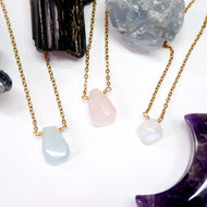 Three gold necklaces with stone pendants on a white surface with crystals.