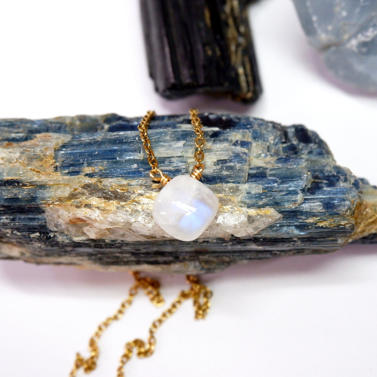 Gold necklace with a white pendant on a rock with crystals in the background