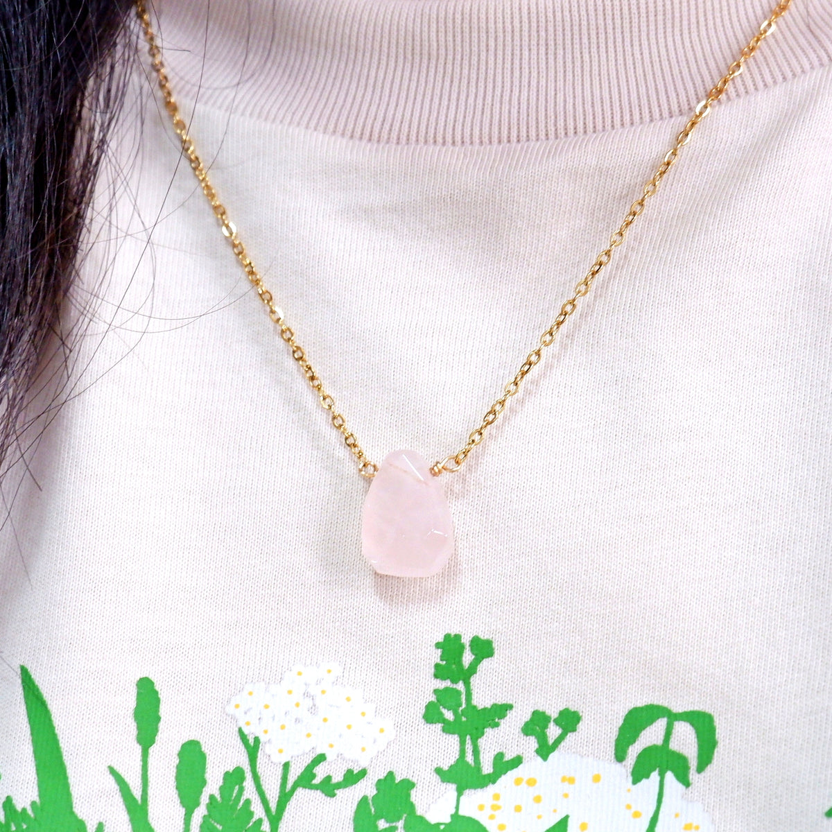 Necklace with a pink pendant worn by a person against a white background with green floral patterns.
