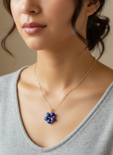 Woman wearing a gold necklace with a blue pendant against a neutral background