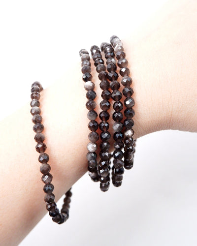 Three dark beaded bracelets on a wrist against a white background