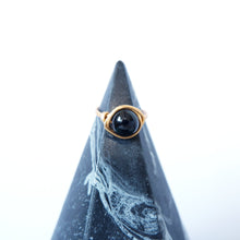 Gold ring with a black gemstone on a textured blue stand against a white background