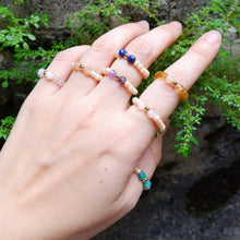 Hand wearing multiple beaded rings with a natural background