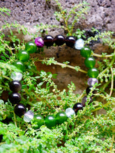 Necklace with green, black, and clear beads lying on green foliage