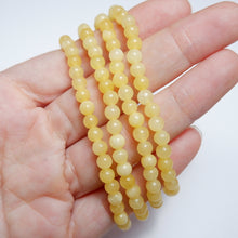 Yellow beaded necklace held in a hand against a white background