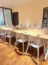 A long light wood conference table with white chairs in a bright meeting room with wood floors and beige walls.