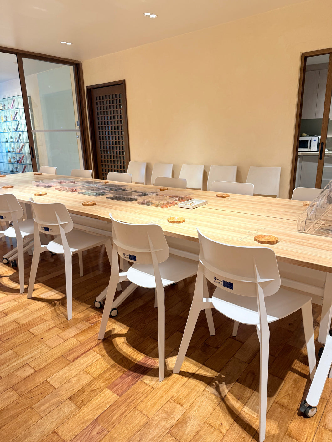 A long light wood conference table with white chairs in a bright meeting room with wood floors and beige walls.