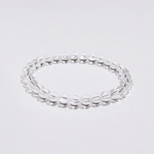 A bracelet made of clear quartz beads strung together on a white garter, displayed against a white background.