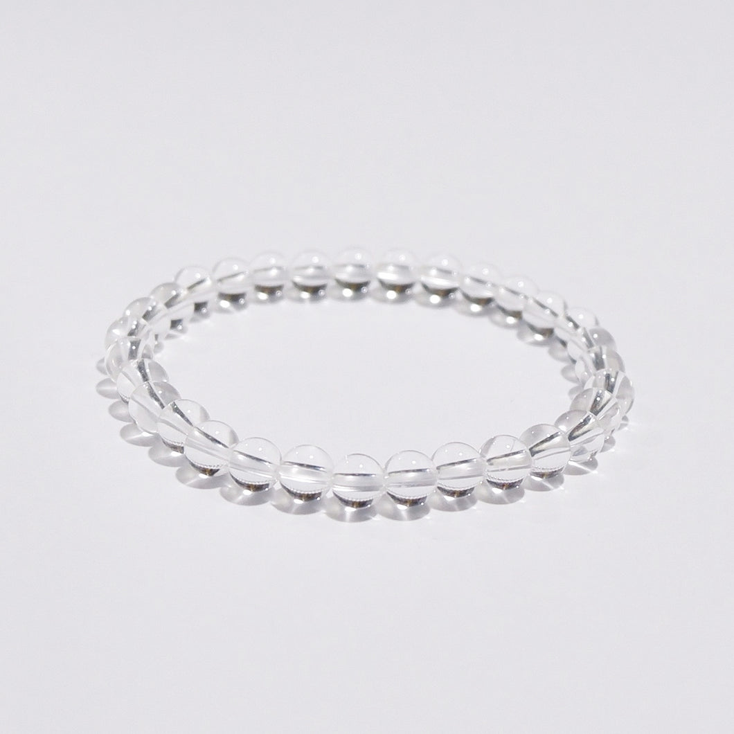 A bracelet made of clear quartz beads strung together on a white garter, displayed against a white background.