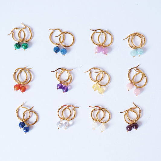 A collection of handmade gold hoop earrings, each with different semi-precious crystal dangles, displayed on a white background.