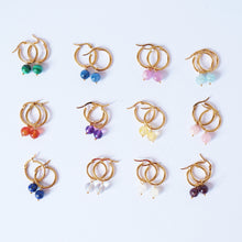 A collection of handmade gold hoop earrings, each with different semi-precious crystal dangles, displayed on a white background.