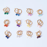 A collection of handmade gold hoop earrings, each with different semi-precious crystal dangles, displayed on a white background.