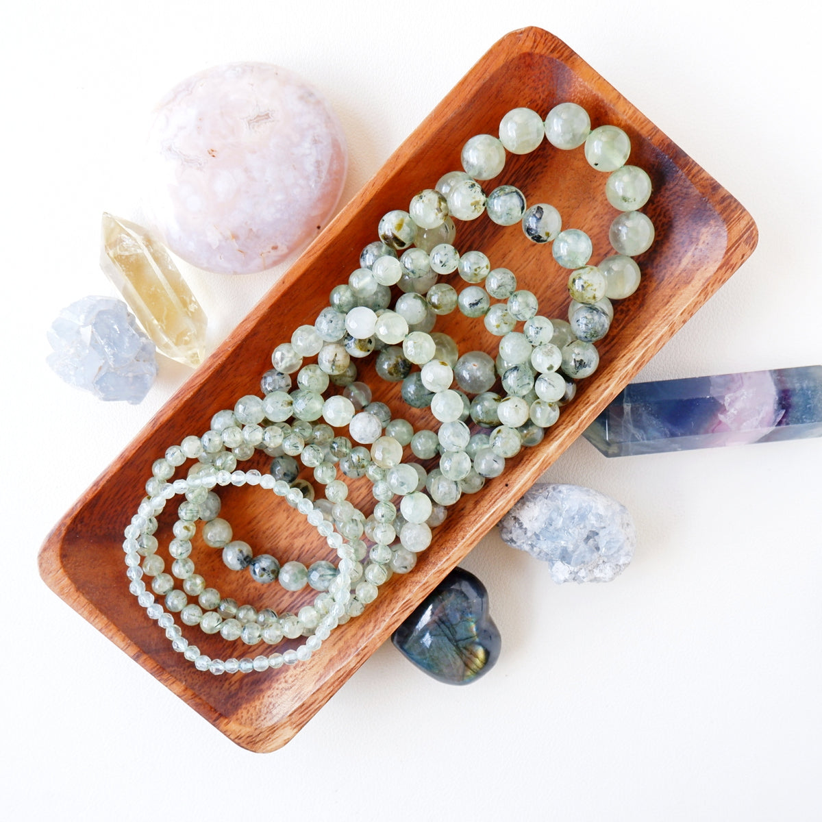 A Prehnite bracelet with a series of round beads in various shades of green, strung together on a wooden bracelet holder.