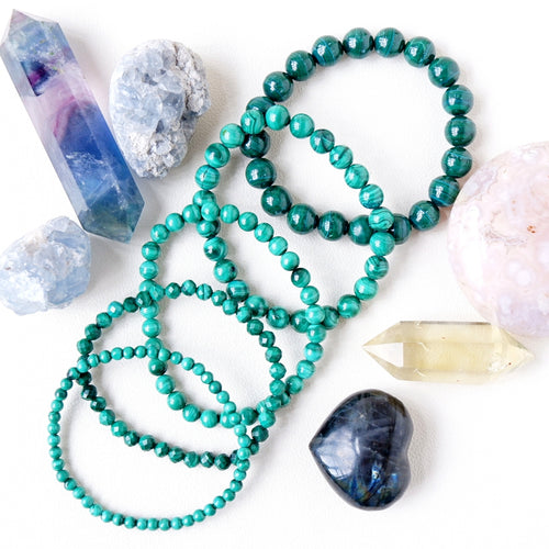 A variety of beaded bracelets in green and other colors, along with crystal stones and a semi-precious stone.