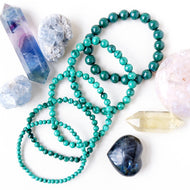 A variety of beaded bracelets in green and other colors, along with crystal stones and a semi-precious stone.